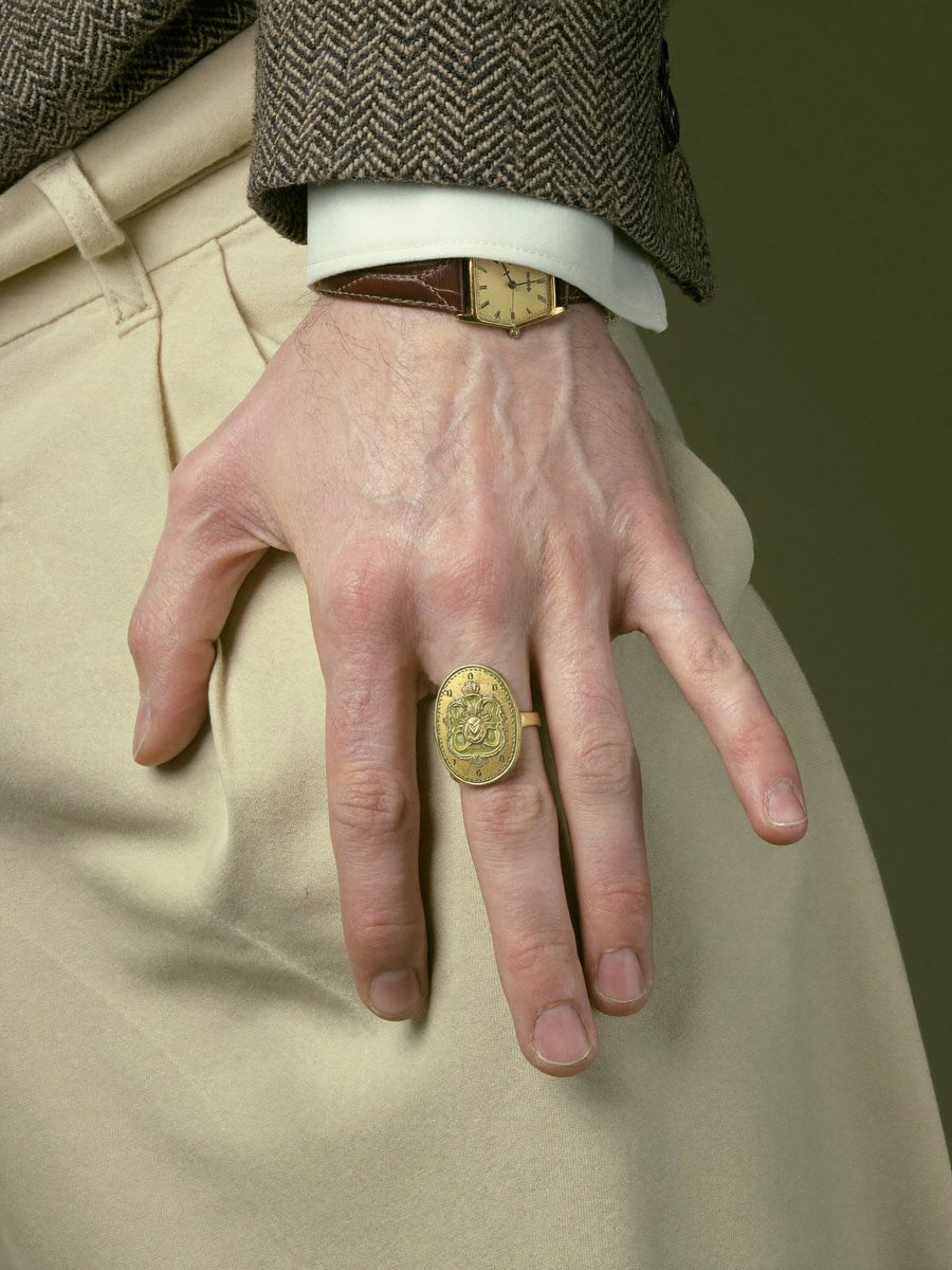 A pale hand on a cream trouser knee, a gold signet ring on one finger