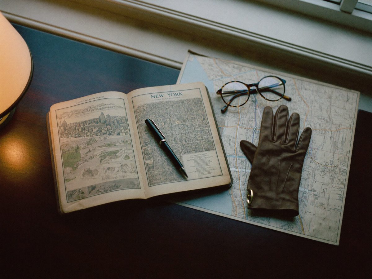 An old New York guidebook and a street map on a desk, with tortoiseshell glasses and a fountain pen