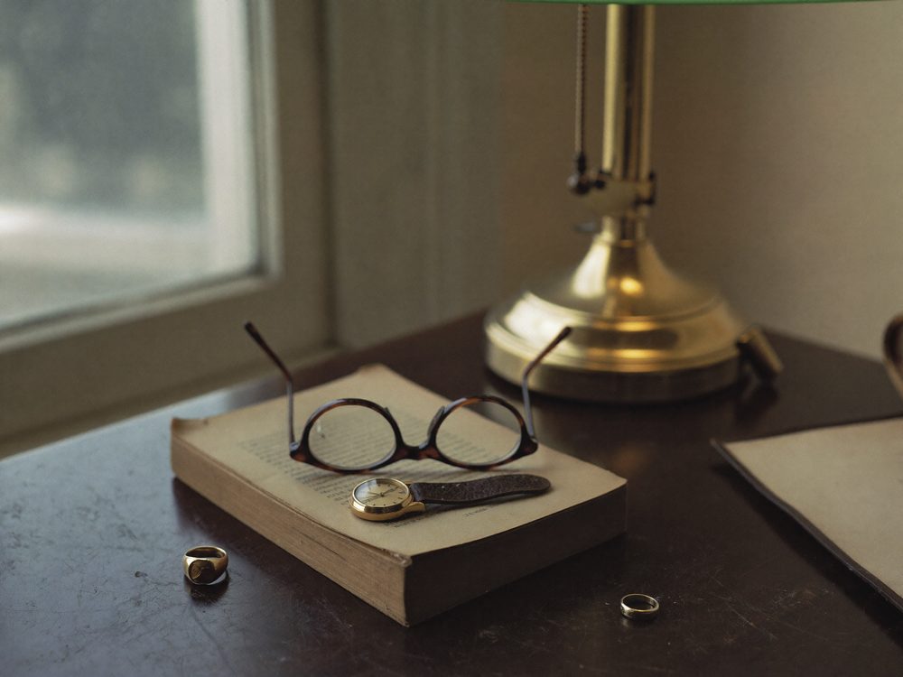 Tortoiseshell glasses, a gold watch and a signet ring on an open book